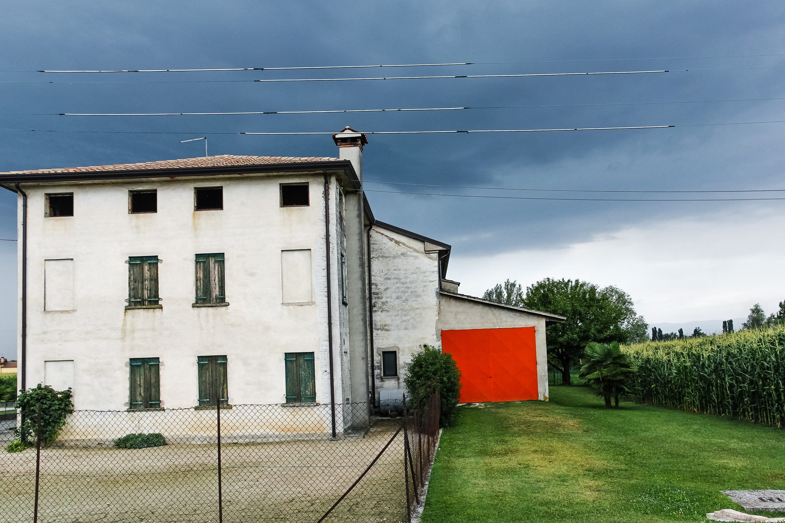 Schwarze Wolken über dem Gehöft, daneben leuchtet das orange Tor
